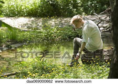 Young woman sitting by river, pikcing wildflowers View Large Photo Image Stock Image - Young woman sitting by river, pikcing wildflowers. Fotosearch