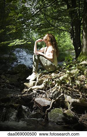 Young woman sitting by stream in woods View Large Photo Image Stock Image - Young woman sitting by stream in woods. Fotosearch