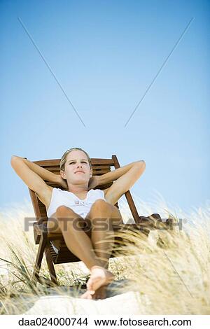 Picture - Young woman sitting in deck chair, in dunes. Fotosearch