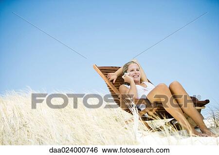 Young woman sitting in deck chair, in dunes, using cell phone View Large Photo Image Stock Photograph - Young woman sitting in deck chair, in dunes, using cell phone. Fotosearch