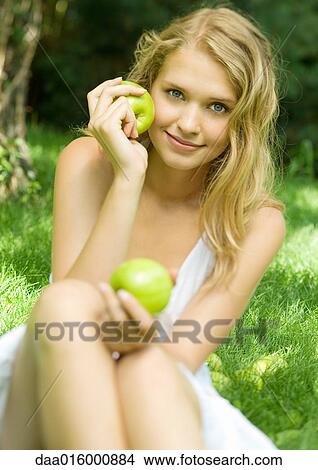 Young woman sitting in grass, holding up apples View Large Photo Image Picture - Young woman sitting in grass, holding up apples. Fotosearch
