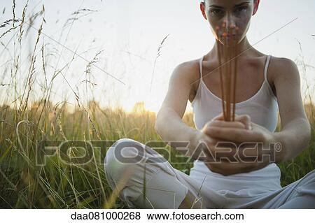 Young woman sitting in grass, holding incense sticks View Large Photo Image Stock Photo - Young woman sitting in grass, holding incense sticks. Fotosearch