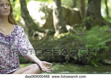 Stock Photo - Young woman sitting in lotus position outdoors. Fotosearch