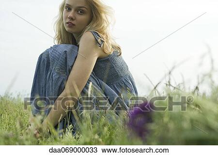 Stock Image - Young woman sitting in meadow, portrait. Fotosearch