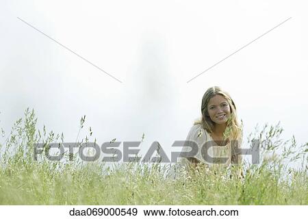 Stock Photo - Young woman sitting in tall grass, portrait. Fotosearch