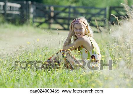 Young woman sitting in tall grass with knees up, smiling at camera View Large Photo Image Stock Photography - Young woman sitting in tall grass with knees up, smiling at camera. Fotosearch