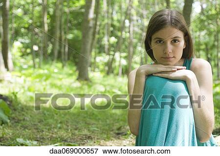 Young woman sitting in woods with chin resting on knees, portrait View Large Photo Image Stock Photo - Young woman sitting in woods with chin resting on knees, portrait. Fotosearch