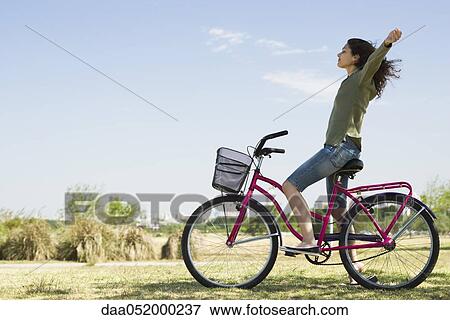 Stock Photo - Young woman sitting on bicycle with arms out and eyes closed. Fotosearch
