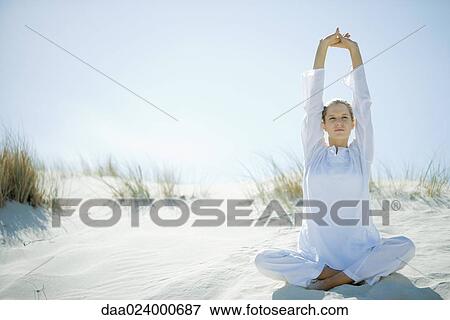 Young woman sitting on dune, stretching arms over head View Large Photo Image Stock Photo - Young woman sitting on dune, stretching arms over head. Fotosearch