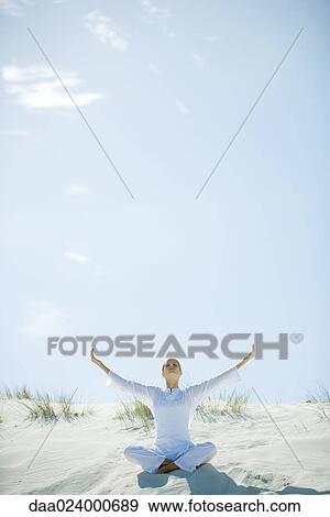 Young woman sitting on dune with eyes closed and arms out, full length View Large Photo Image Stock Photo - Young woman sitting on dune with eyes closed and arms out, full length. Fotosearch