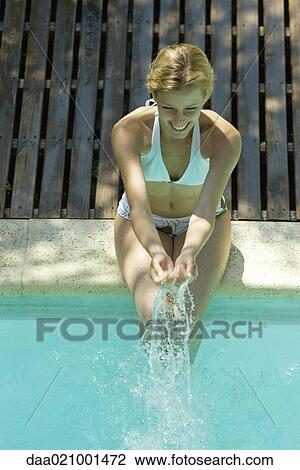 Young woman sitting on edge of pool, splashing water View Large Photo Image Stock Image - Young woman sitting on edge of pool, splashing water. Fotosearch