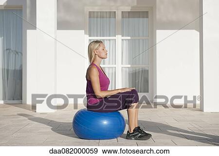 Stock Photo - Young woman sitting on fitness ball with eyes closed. Fotosearch
