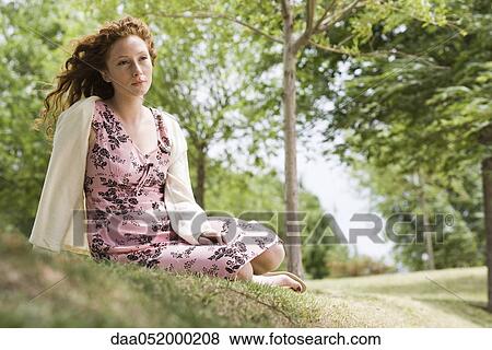 Young woman sitting on grass, looking away in thought View Large Photo Image Stock Photo - Young woman sitting on grass, looking away in thought. Fotosearch