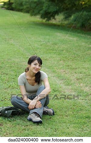 Young woman sitting on grass, smiling at camera View Large Photo Image Stock Image - Young woman sitting on grass, smiling at camera. Fotosearch
