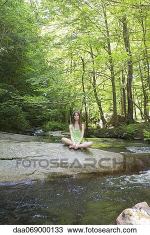 Young woman sitting on rock beside stream View Large Photo Image Stock Image - Young woman sitting on rock beside stream. Fotosearch