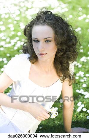 Picture - Young woman sitting on the ground, holding flowers, looking at camera. Fotosearch
