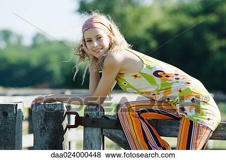 Young woman sitting on top of wooden fence, leaning on elbow, smiling at camera View Large Photo Image Stock Photo - Young woman sitting on top of wooden fence, leaning on elbow, smiling at camera. Fotosearch