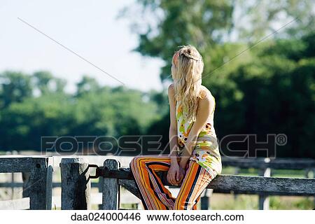 Young woman sitting on top of wooden fence, looking over shoulder View Large Photo Image Stock Photograph - Young woman sitting on top of wooden fence, looking over shoulder. Fotosearch