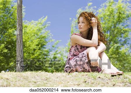 Young woman sitting outdoors, looking away in thought View Large Photo Image Picture - Young woman sitting outdoors, looking away in thought. Fotosearch