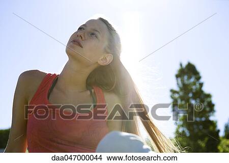 Young woman sitting outdoors, looking up View Large Photo Image Picture - Young woman sitting outdoors, looking up. Fotosearch
