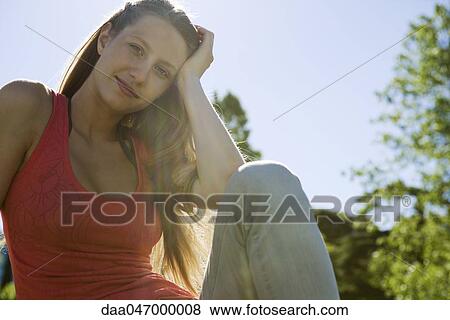 Young woman sitting outdoors on sunny day, smiling, portrait View Large Photo Image Stock Photo - Young woman sitting outdoors on sunny day, smiling, portrait. Fotosearch