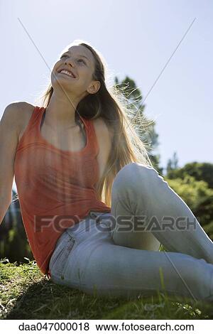 Young woman sitting outdoors on sunny day, looking up and smiling View Large Photo Image Stock Photo - Young woman sitting outdoors on sunny day, looking up and smiling. Fotosearch