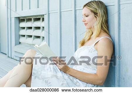 Young woman sitting outdoors, reading book, side view View Large Photo Image Stock Photograph - Young woman sitting outdoors, reading book, side view. Fotosearch