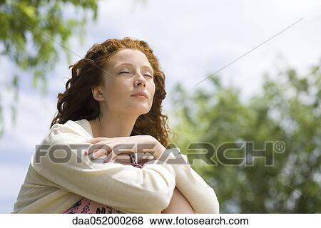 Stock Photo - Young woman sitting outdoors with eyes closed. Fotosearch