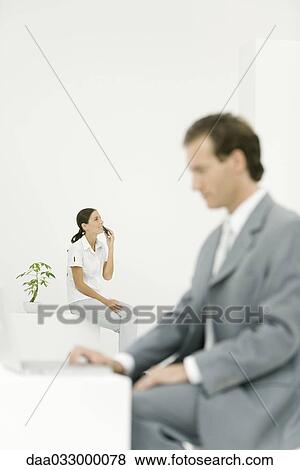 Stock Photo - Young woman sitting with cell phone, professional man using laptop computer in foreground. Fotosearch