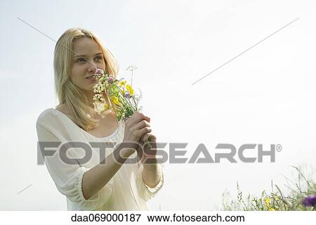 Stock Photo - Young woman smelling bouquet of wildflowers. Fotosearch