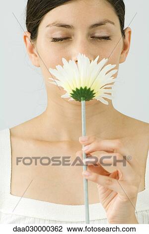 Stock Image - Young woman smelling flower, eyes closed, portrait. Fotosearch