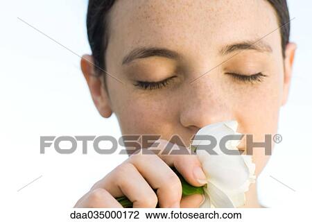 Stock Image - Young woman smelling white rose blossom, eyes closed, close-up. Fotosearch