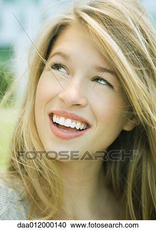 Stock Image - Young woman smiling and looking up, portrait. Fotosearch