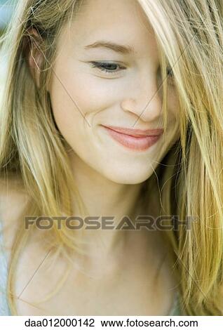 Stock Image - Young woman smiling, hair covering one eye, portrait. Fotosearch