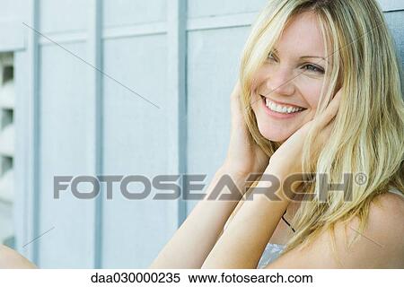 Stock Photography - Young woman smiling, hands over ears. Fotosearch