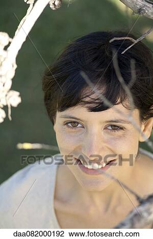 Young woman smiling through tree branches, portrait View Large Photo Image Stock Image - Young woman smiling through tree branches, portrait. Fotosearch