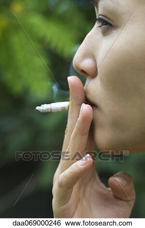 Stock Photograph - Young woman smoking outdoors, side view. Fotosearch