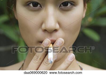 Stock Image - Young woman smoking outdoors. Fotosearch