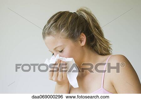 Stock Photograph - Young woman sneezing into tissue. Fotosearch