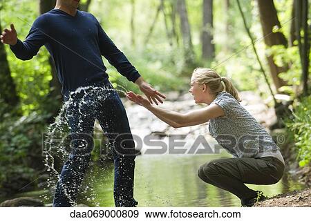 Stock Photo - Young woman splashing water at man. Fotosearch