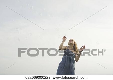 Stock Photo - Young woman standing among floating bubbles. Fotosearch
