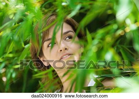Young woman standing among foliage, looking up View Large Photo Image Stock Photograph - Young woman standing among foliage, looking up. Fotosearch