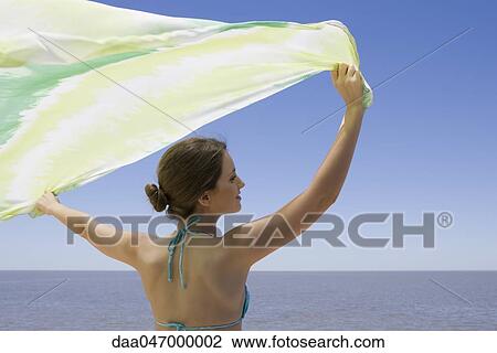 Young woman standing before sea, holding scarf in breeze View Large Photo Image Stock Image - Young woman standing before sea, holding scarf in breeze. Fotosearch