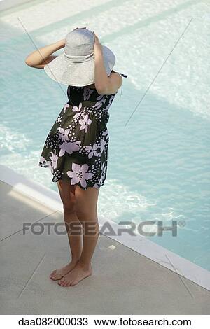 Young woman standing beside pool, putting on sun hat View Large Photo Image Stock Image - Young woman standing beside pool, putting on sun hat. Fotosearch