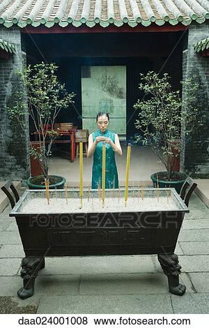 Young woman standing by censer, holding up incense in temple courtyard View Large Photo Image Stock Photo - Young woman standing by censer, holding up incense in temple courtyard. Fotosearch