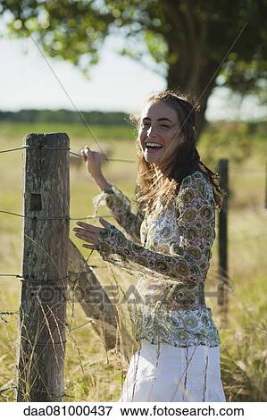 Young woman standing by fence in field View Large Photo Image Stock Photo - Young woman standing by fence in field. Fotosearch