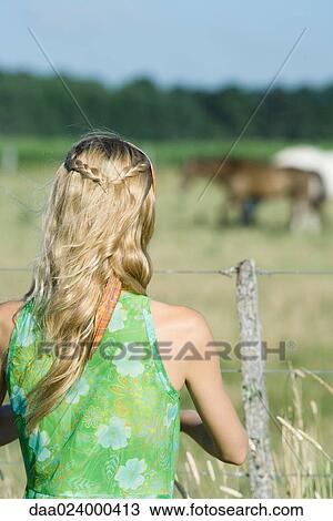 Young woman standing by fence in rural field, rear view View Large Photo Image Stock Image - Young woman standing by fence in rural field, rear view. Fotosearch