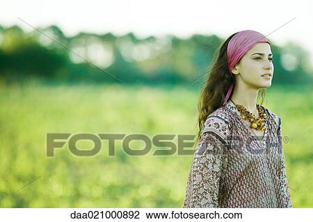 Young woman standing by field, looking into distance View Large Photo Image Stock Image - Young woman standing by field, looking into distance. Fotosearch