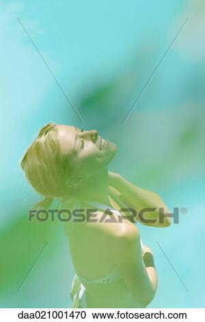 Stock Image - Young woman standing in bikini, eyes closed, high angle view, blur in foreground. Fotosearch