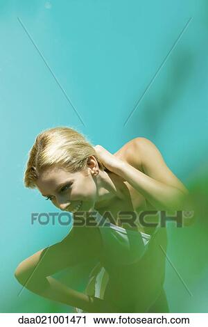 Stock Image - Young woman standing in bikini with hand on neck, high angle view, blur in foreground. Fotosearch